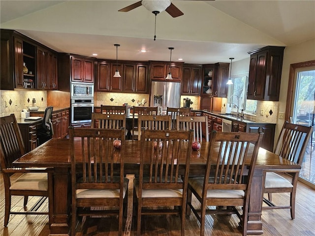 dining room with ceiling fan, hardwood / wood-style floors, vaulted ceiling, and sink