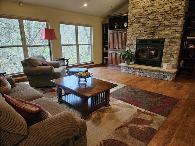 living room featuring hardwood / wood-style flooring, a stone fireplace, and lofted ceiling