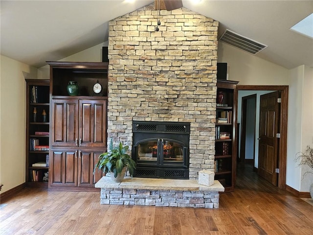 unfurnished living room with wood-type flooring, a stone fireplace, and lofted ceiling