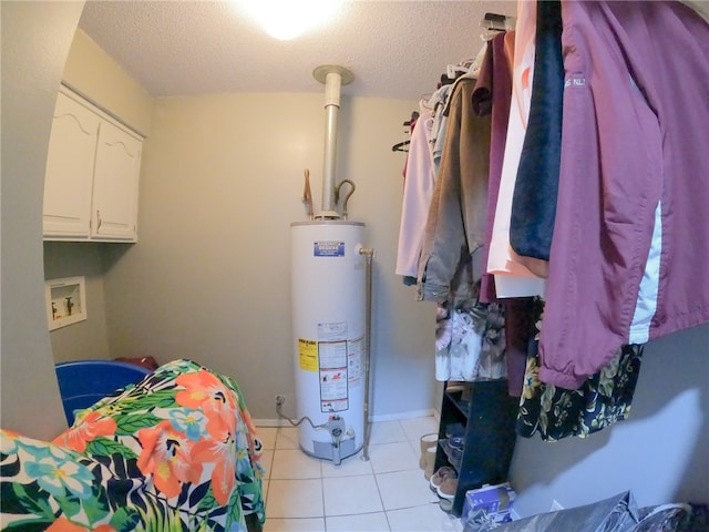 laundry area featuring water heater, cabinets, a textured ceiling, and light tile patterned floors