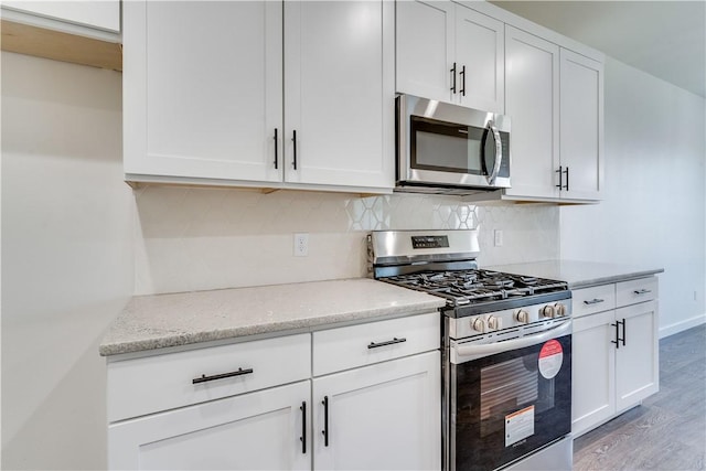 kitchen featuring appliances with stainless steel finishes, light hardwood / wood-style flooring, white cabinetry, and light stone counters