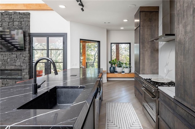 514 N Vinson Ave, Fayetteville, AR 72701 - kitchen with wall chimney range hood, high end stainless steel range oven, a sink, dark brown cabinetry, and dark stone counters