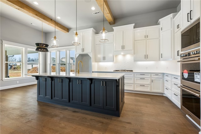 kitchen with a kitchen island with sink, beam ceiling, decorative light fixtures, dark hardwood / wood-style floors, and white cabinetry