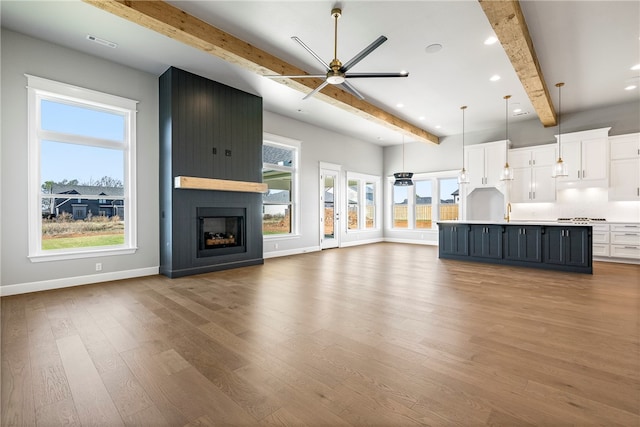 unfurnished living room with light wood-type flooring, a large fireplace, ceiling fan, sink, and beamed ceiling