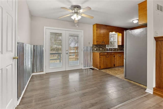kitchen with a ceiling fan, a sink, brown cabinetry, french doors, and freestanding refrigerator