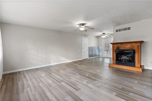 unfurnished living room featuring a ceiling fan, wood finished floors, a fireplace with raised hearth, baseboards, and visible vents