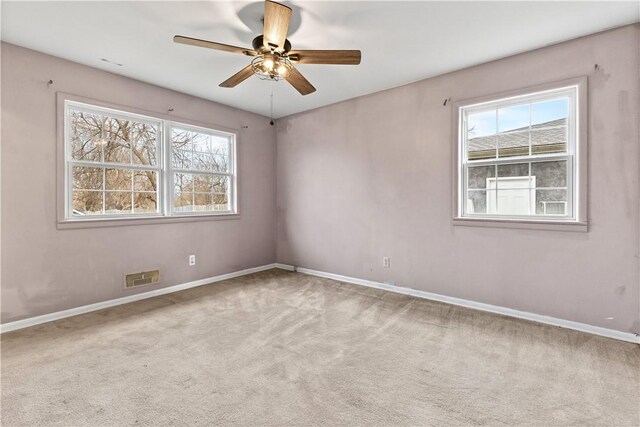 carpeted empty room featuring visible vents, a ceiling fan, and baseboards