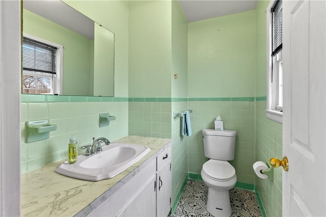 bathroom featuring tile patterned floors, toilet, wainscoting, tile walls, and vanity