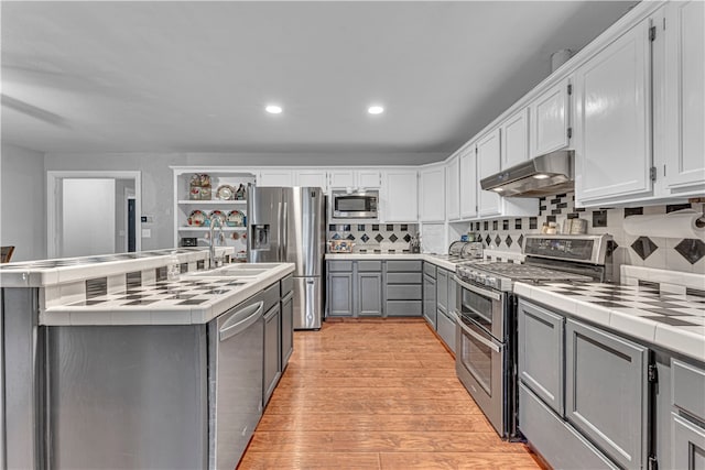 kitchen featuring tile countertops, a kitchen island with sink, light hardwood / wood-style flooring, tasteful backsplash, and stainless steel appliances