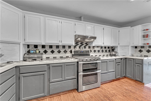 kitchen with gray cabinets, tile countertops, range with two ovens, and light hardwood / wood-style flooring