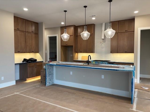 kitchen featuring sink, a center island with sink, decorative backsplash, and decorative light fixtures