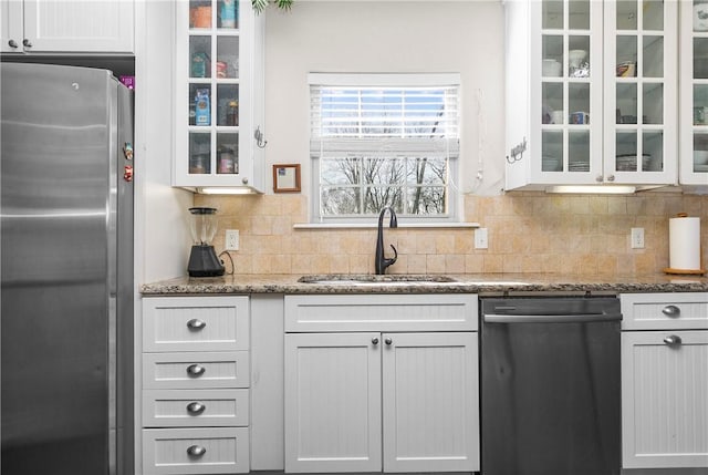 kitchen with appliances with stainless steel finishes, tasteful backsplash, sink, stone counters, and white cabinetry