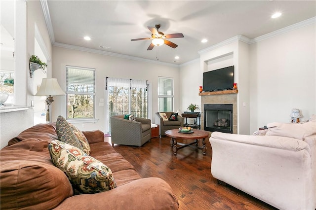 living room with a tile fireplace, ornamental molding, ceiling fan, and dark wood-type flooring