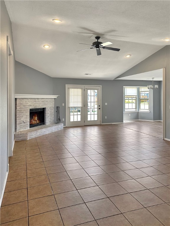 unfurnished living room featuring ceiling fan with notable chandelier, a textured ceiling, light tile patterned floors, a fireplace, and lofted ceiling