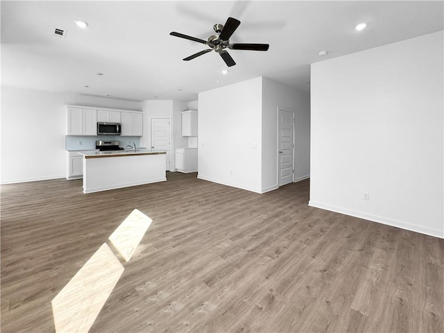 unfurnished living room with baseboards, light wood finished floors, recessed lighting, a sink, and ceiling fan