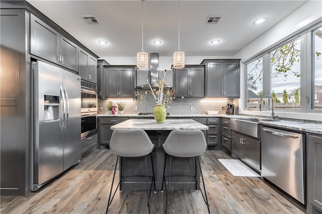 kitchen with hanging light fixtures, a center island, stainless steel appliances, and light hardwood / wood-style floors