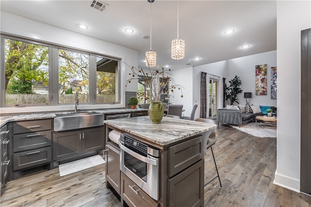 kitchen featuring light stone counters, sink, wood-type flooring, decorative light fixtures, and a breakfast bar area