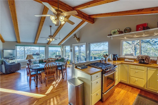 kitchen with vaulted ceiling with beams, stainless steel range with gas cooktop, kitchen peninsula, ceiling fan, and light hardwood / wood-style flooring