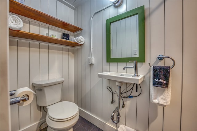 bathroom featuring toilet, wooden walls, sink, and tile patterned floors