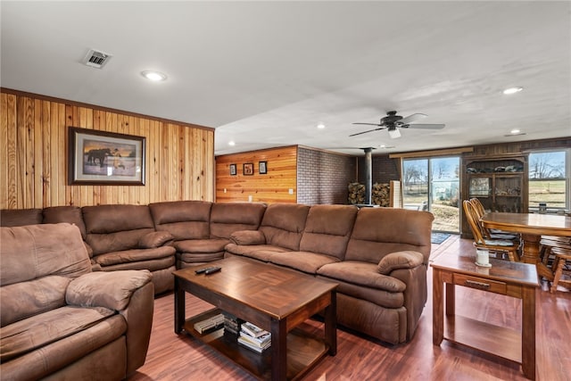 living room with wood-type flooring, a wood stove, ceiling fan, and wooden walls