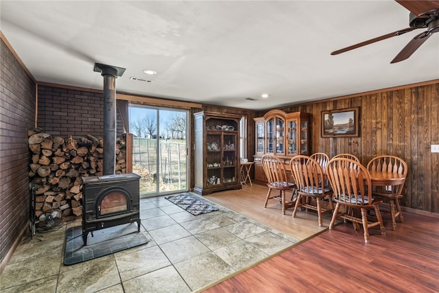 dining room featuring a wood stove, wood walls, ceiling fan, and hardwood / wood-style flooring