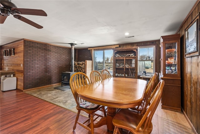 dining room with hardwood / wood-style floors, a wood stove, wooden walls, and brick wall