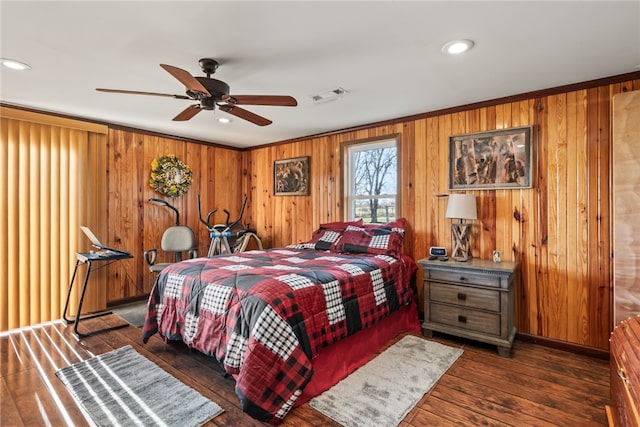 bedroom with ceiling fan, crown molding, dark wood-type flooring, and wood walls