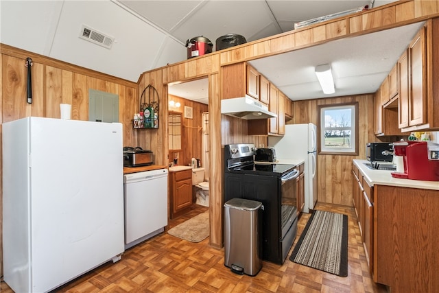 kitchen with white appliances, vaulted ceiling, light parquet flooring, and wood walls