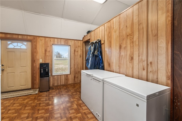 clothes washing area with washing machine and clothes dryer, dark parquet flooring, and wood walls