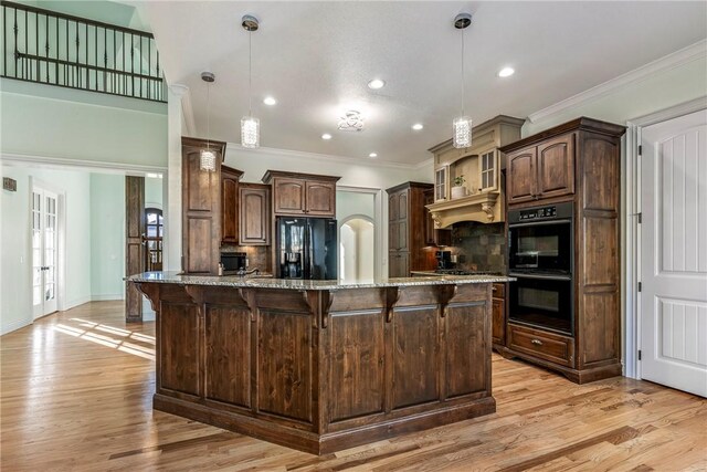 kitchen featuring light hardwood / wood-style floors, black appliances, a center island with sink, and light stone counters