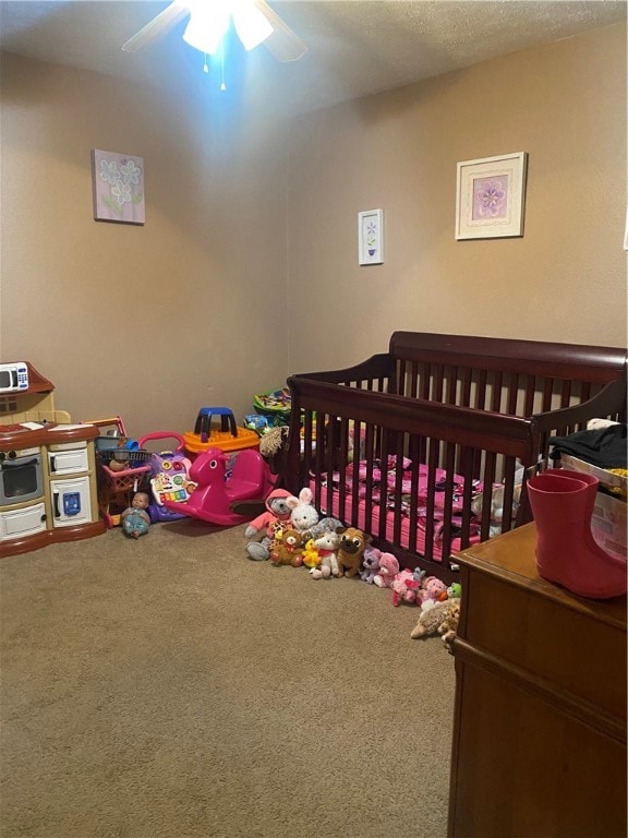 carpeted bedroom featuring a textured ceiling, ceiling fan, and a crib