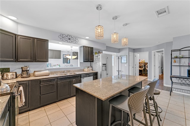 kitchen featuring a breakfast bar, dark brown cabinets, a kitchen island, light stone counters, and stainless steel appliances