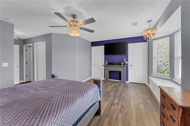 bedroom featuring ceiling fan with notable chandelier, wood-type flooring, and a brick fireplace