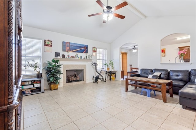 tiled living room with lofted ceiling with beams, a tiled fireplace, and ceiling fan