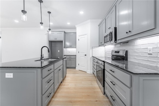 kitchen featuring a kitchen island with sink, sink, dark stone countertops, appliances with stainless steel finishes, and decorative light fixtures