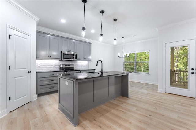 kitchen with appliances with stainless steel finishes, sink, a center island with sink, decorative light fixtures, and gray cabinets