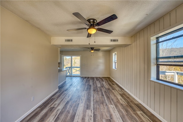 unfurnished room with dark hardwood / wood-style flooring, a wealth of natural light, a textured ceiling, and ceiling fan