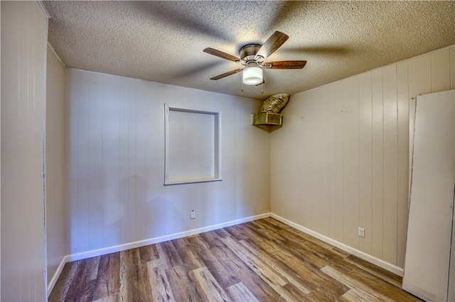 spare room featuring wooden walls, a textured ceiling, ceiling fan, and light hardwood / wood-style flooring