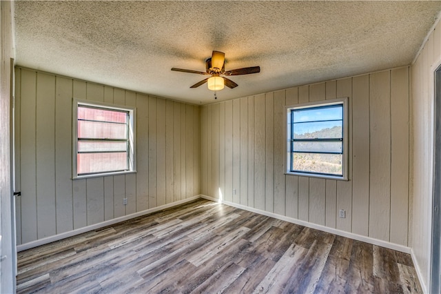 empty room featuring hardwood / wood-style floors, ceiling fan, a textured ceiling, and wooden walls