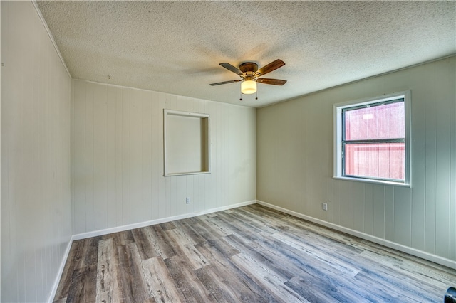 empty room featuring light wood-type flooring, wooden walls, a textured ceiling, and ceiling fan