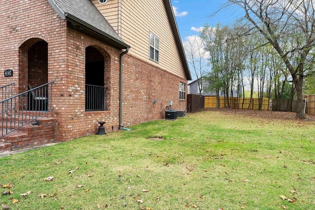 view of home's exterior featuring roof with shingles, brick siding, a yard, fence, and cooling unit