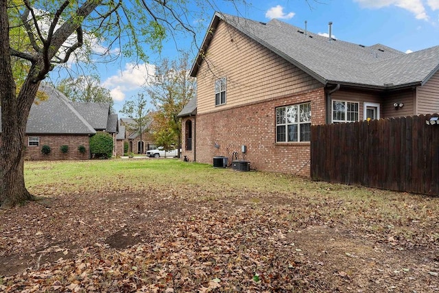 view of home's exterior with a shingled roof, a lawn, fence, cooling unit, and brick siding