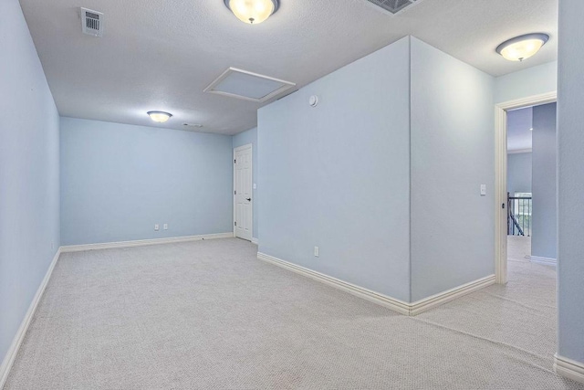 carpeted spare room with attic access, a textured ceiling, visible vents, and baseboards