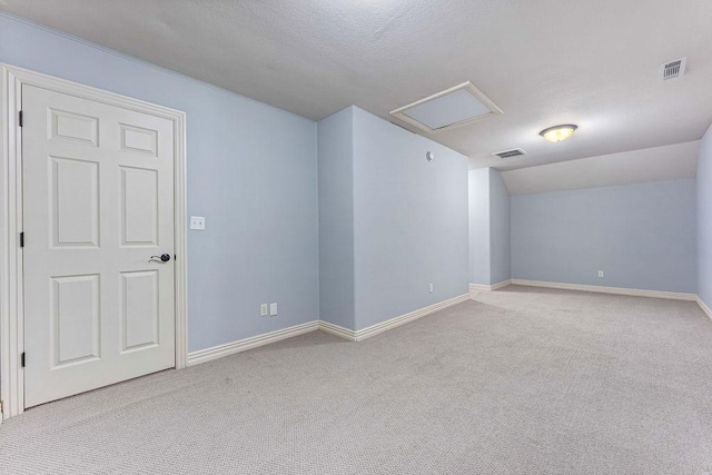 carpeted spare room featuring attic access, lofted ceiling, visible vents, and baseboards