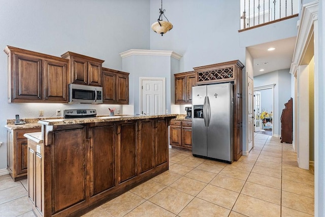 kitchen with light tile patterned floors, a kitchen island, hanging light fixtures, light stone countertops, and stainless steel appliances