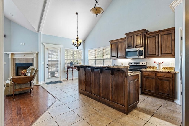 kitchen with light tile patterned flooring, a tile fireplace, stainless steel appliances, light stone countertops, and pendant lighting