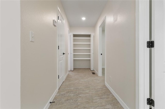 hall with stone finish flooring, visible vents, and baseboards