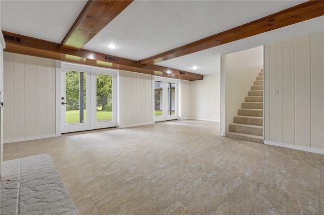 unfurnished living room with beam ceiling, wooden walls, visible vents, and stairs