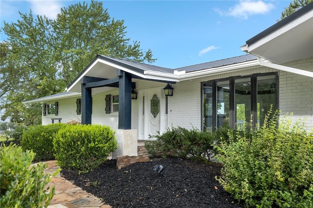 property entrance featuring metal roof, covered porch, and brick siding