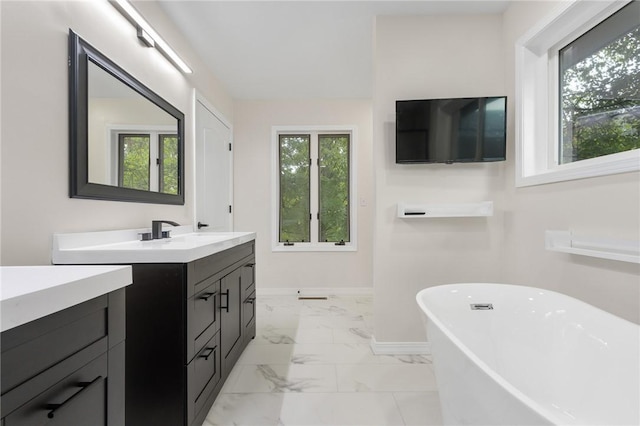 full bathroom featuring vanity, a freestanding bath, marble finish floor, and baseboards